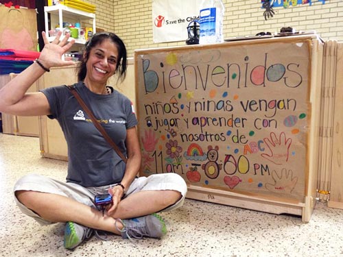 A volunteer sits next to a sign written in Spanish to welcome the children