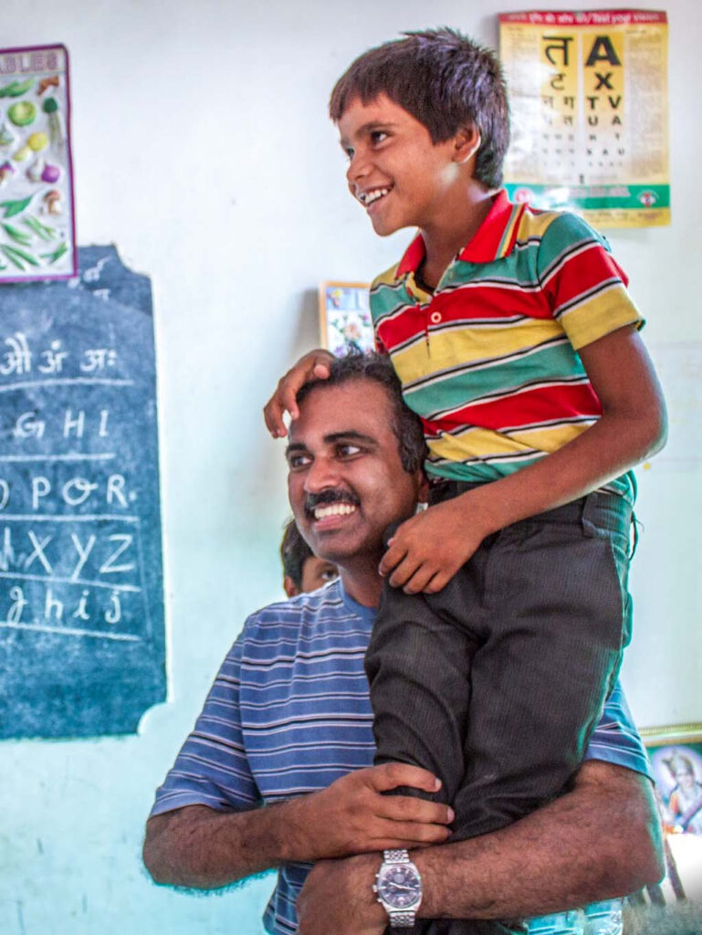 With great affection, a father holds his son up on his shoulder. Both have big smiles.