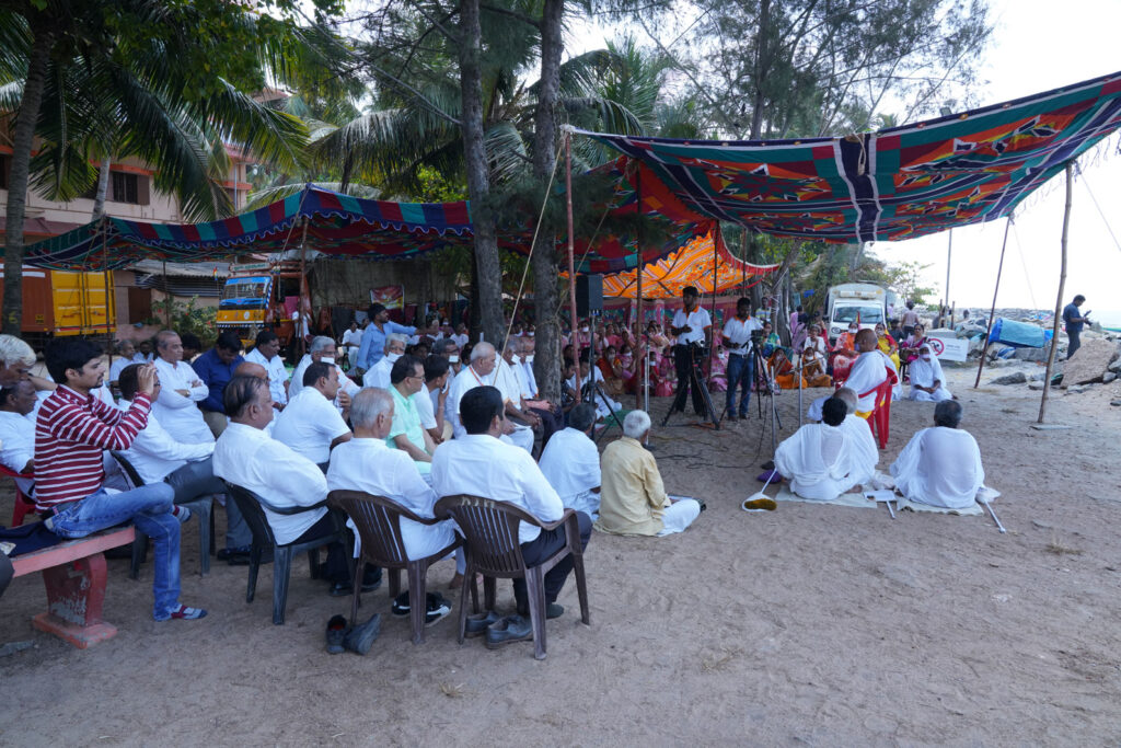 people in chairs at the beach listening to a talk by a man.