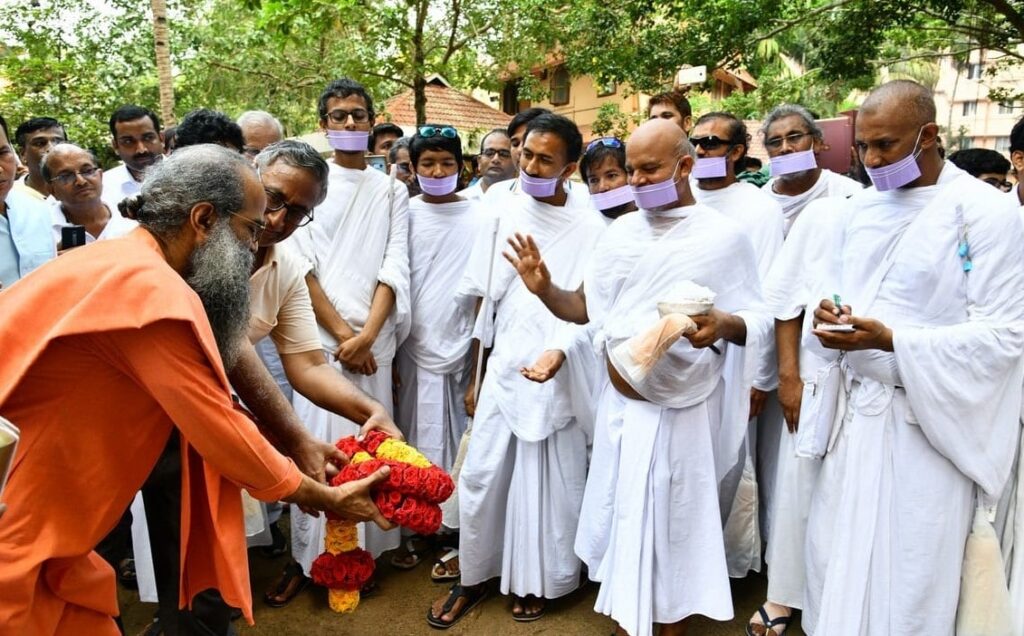 Swami Sudhirananda waves a flame infront of H. H. Acharya surrounded by a group of men.