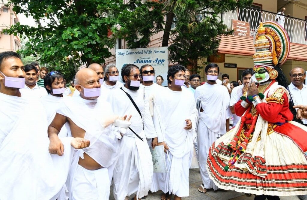 members of the yatra walking past a man dressed in traditional kathakali dress