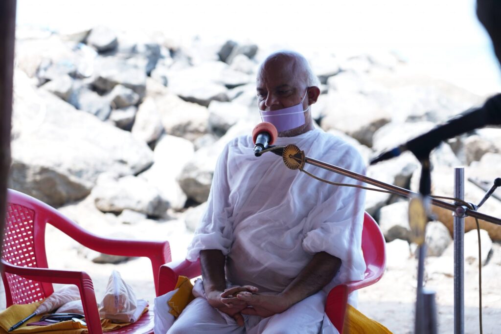 H.H. Acharya sitting in a chair talking into a microphone.