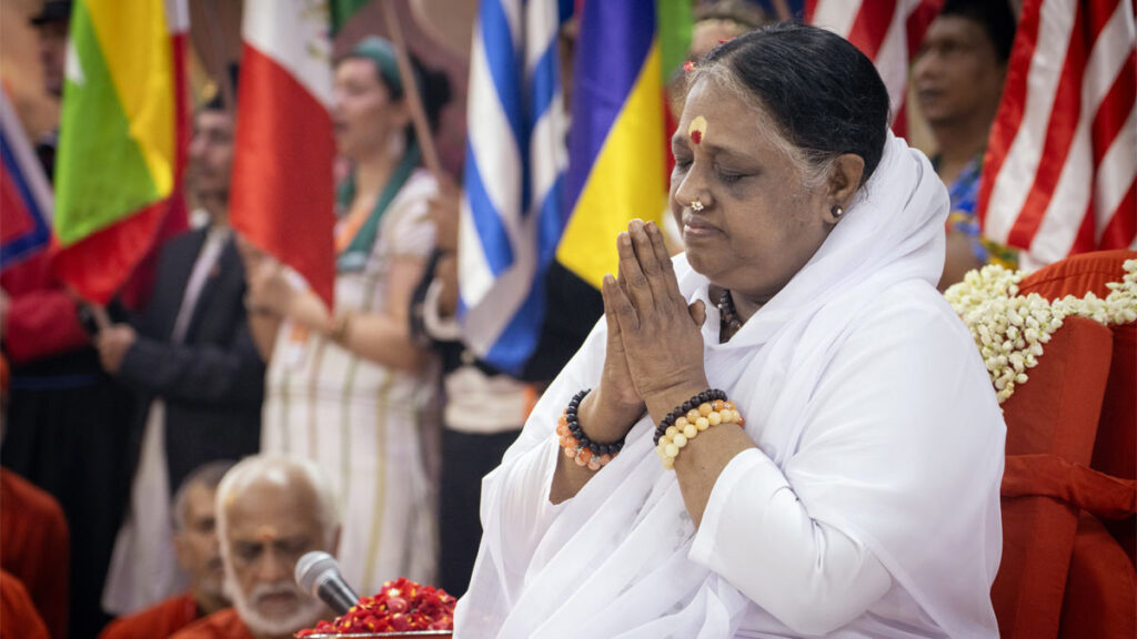 Amma holds her hands in prayer, while flags from many countries are held behind her
