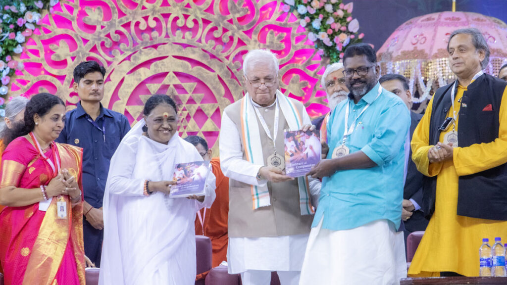 Amma holds up the new book, alongside the dignitaries who are launching it