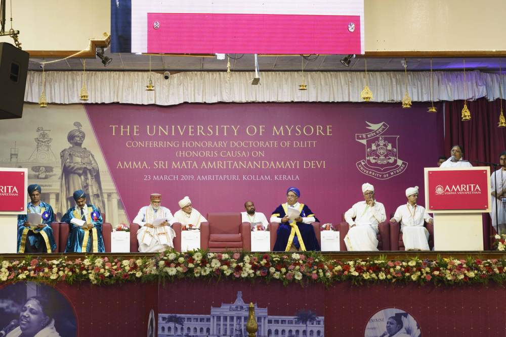 Amma speaking on sage at the ceremony while dignitaries are seated.