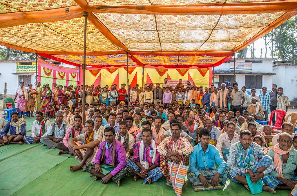 a group of approx 200 farmers seated below a tent with another large group of approx 100 people standing in the background