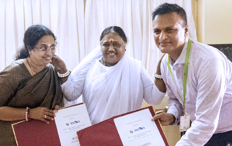 Amma stands with Dr. Kumar and Dr. Ramesh who hold up the signed MoU.