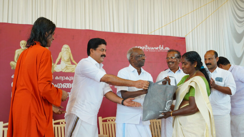 Roshi Augustine, Kerala's Water Resources Minister, hands a bag of supplies to a SGH member.