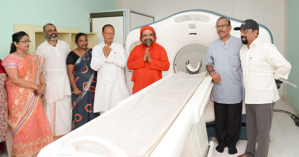 Swami Purnamritananda Puri stands next to the new CT scanner.