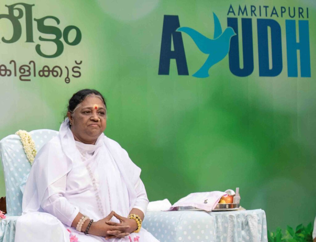 Amma sits in a chair and smiles in front of a green background