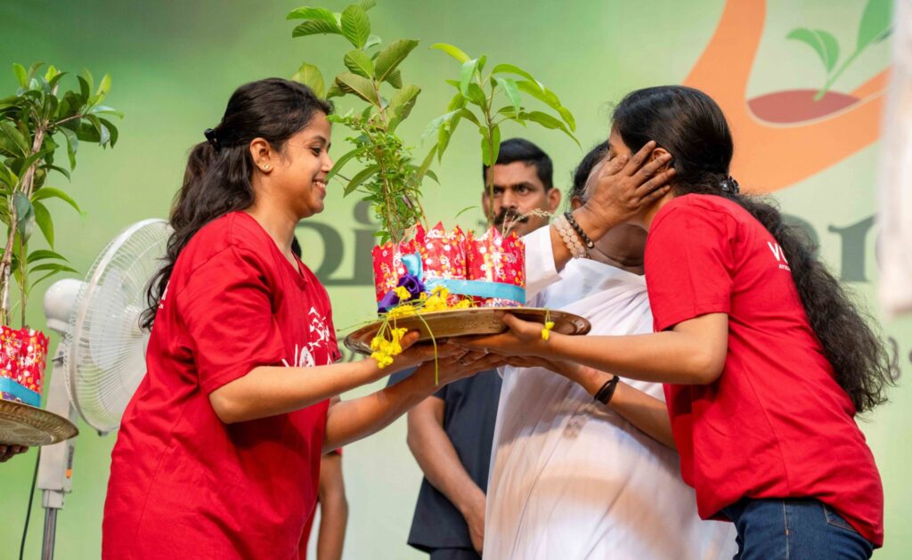 Amma kisses the cheek of an ayudh member who is holding saplings