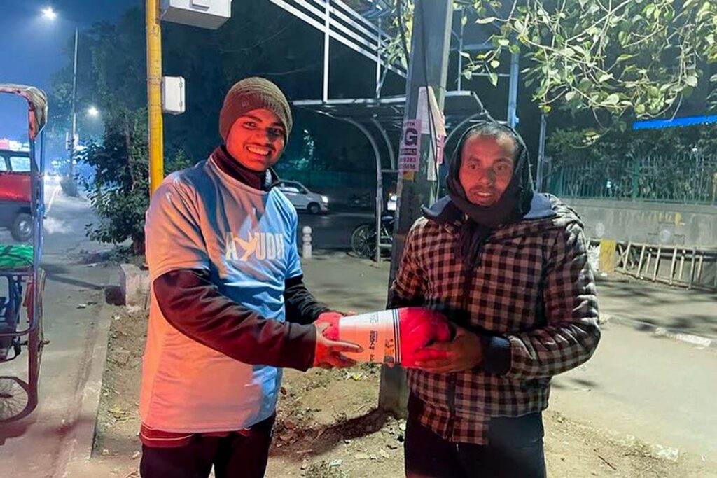A volunteer hands a blanket to a man in Delhi streets