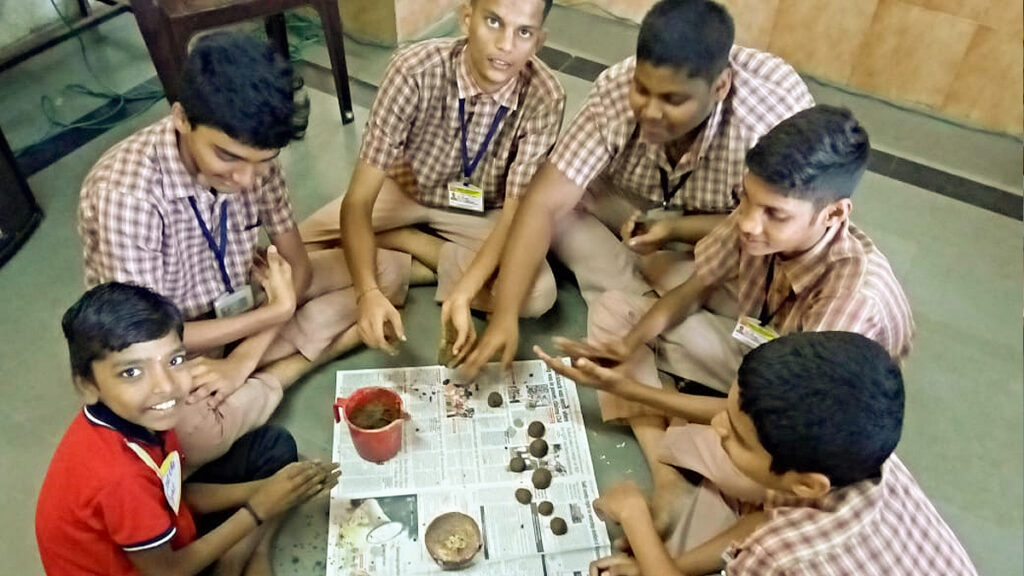 Six young boys sit on the floor and roll seed balls