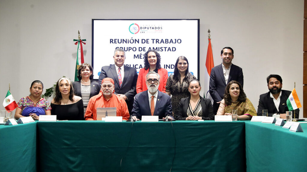 Mexico-Republic of India Friendship Group with Swami Dayamritananda seated at green cloth table with Mexican and Indian flags on each side.