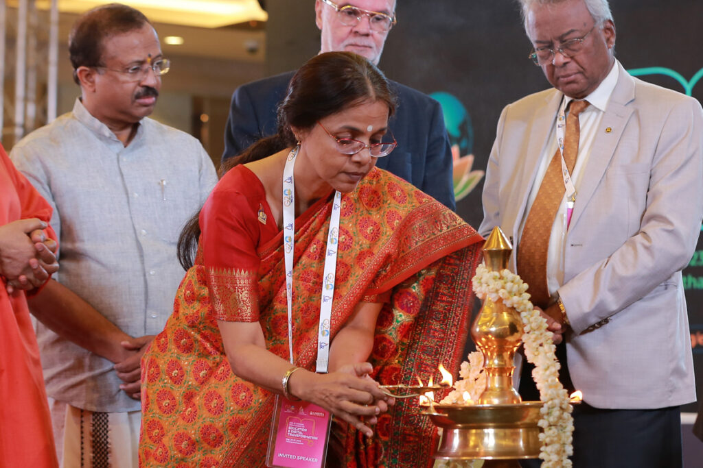 Dr Prema Nedungadi, in a beautiful gold and red sari, mindfully lights the  three foot high Arati lamp. 