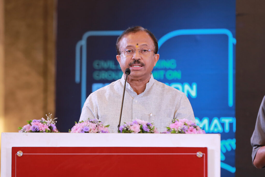 Sri V Muraleedharan, in a light grey shirt at the podium facing front, delivers statistics that currently 41 cities, 12,300 delegates from 110 nationalities have participated.