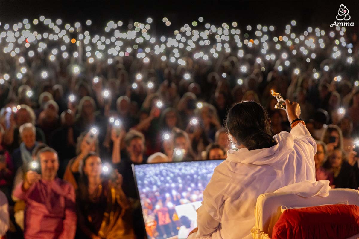 Amma waves an oil lamp to a crowd shining flashlights