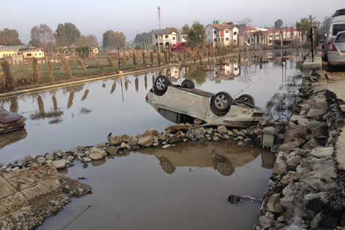 A car is turned upside down next to a flooded area