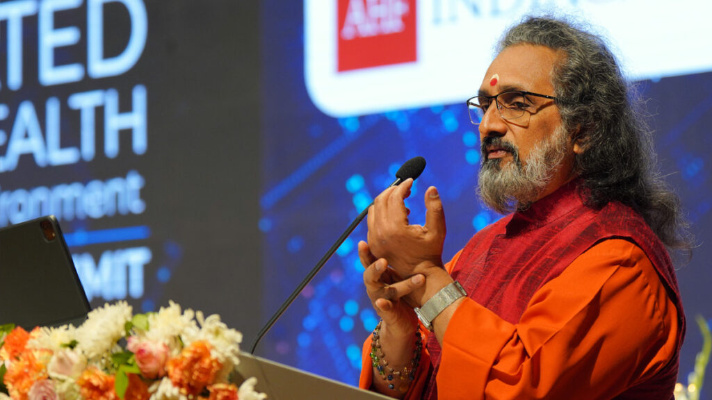 Swami Amritaswarupananda Puri speaking at the podium said to improve our healthcare systems as a society, we can return to traditional spiritual practices to strengthen internal well-being.