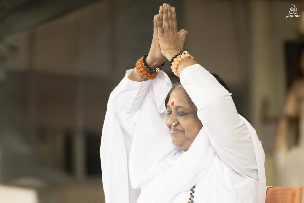 Amma smiles while raising her hands above her head in namaskar