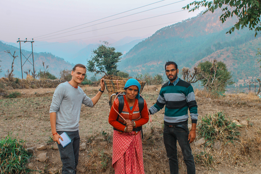 Village woman wears load carrying assistance, and stands between two Amrita University volunteers