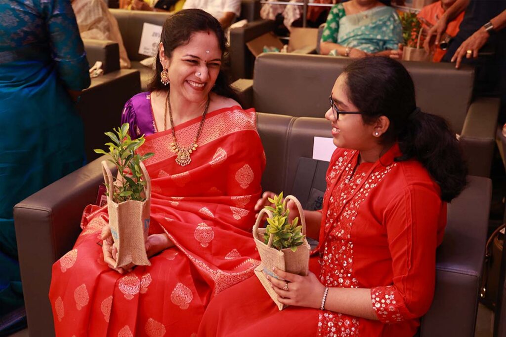 two women hold saplings with smiles on their faces