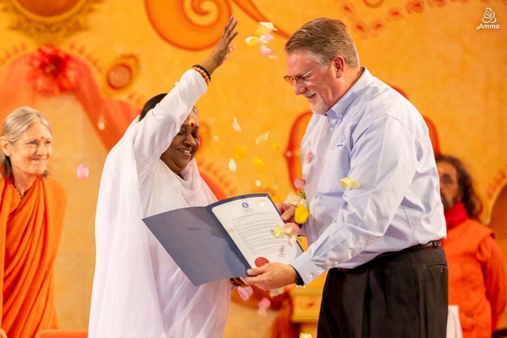 Amma throws petals on a document a man holds