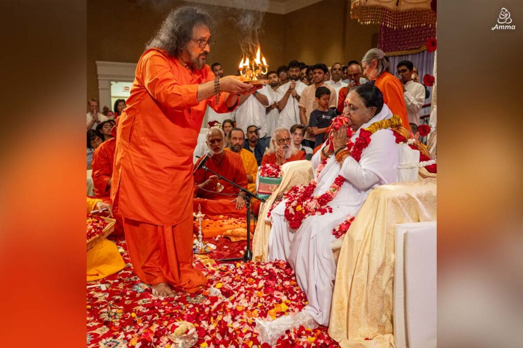 A Swami waves a lamp to Amma