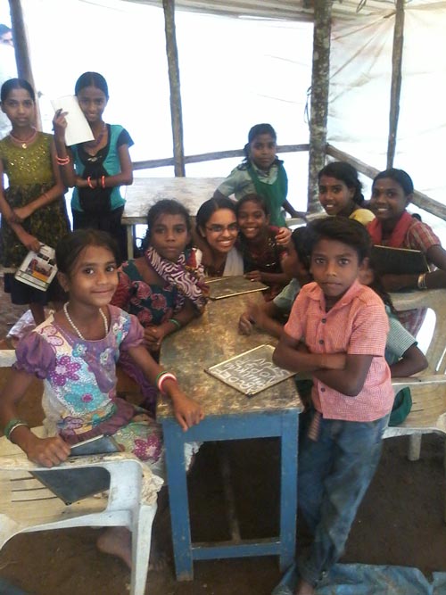 A group of children gather at a desk and smile at the camera