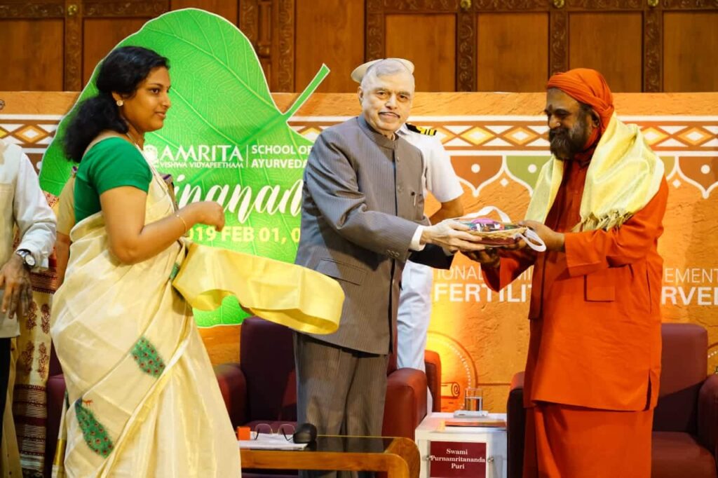 Hon. Kerala Governor (Retd.) Justice P. Sadasivam hands Swami Poornamritananda an item as part of the inaugral ceremony.