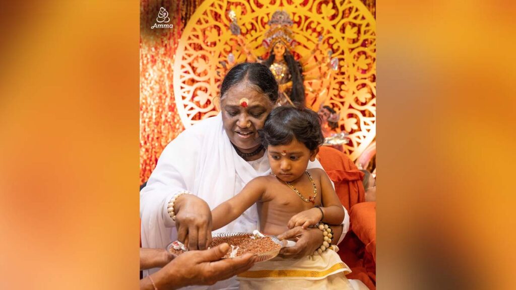 Amma traces a child's finger in rice