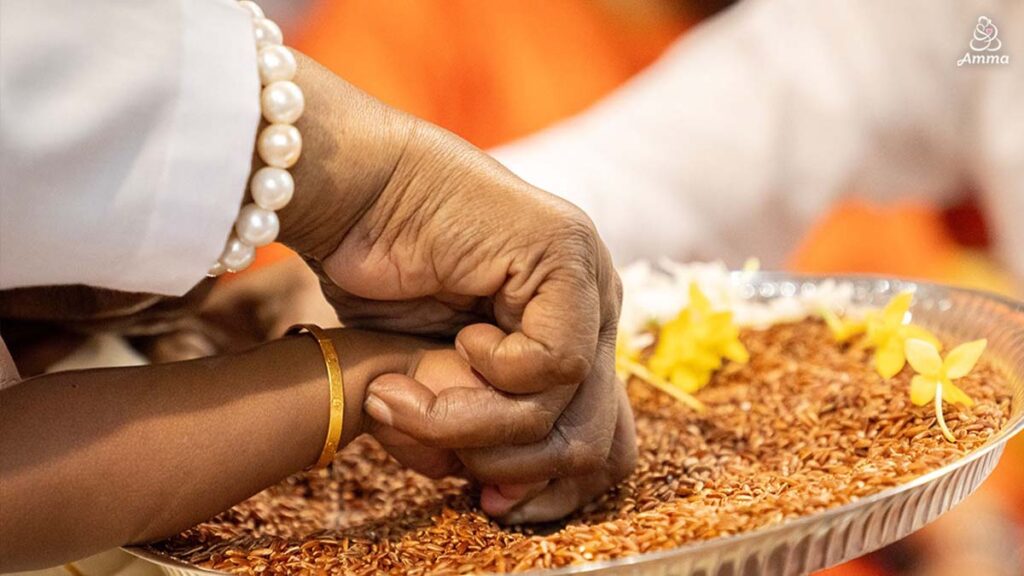 Amma traces a child's finger in rice