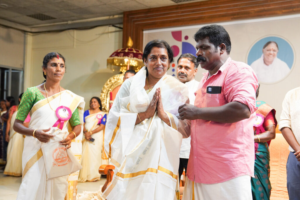 An alumni woman honored and adorned with a traditional Kerala cloth, pranams in gratitude.