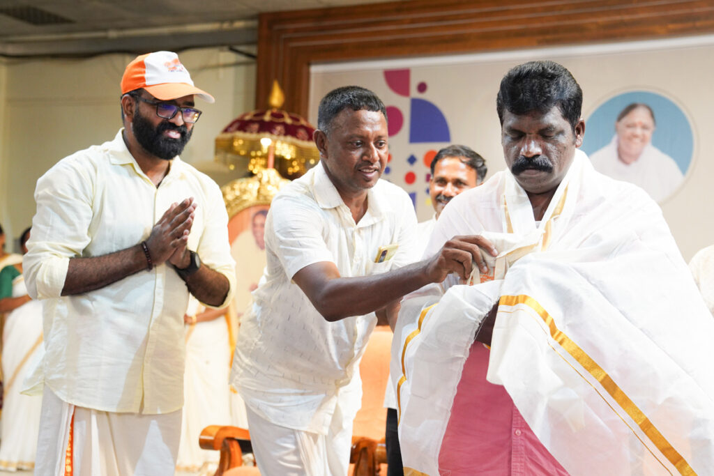 Two men help adorn and gift an honored alumni with the traditional Kerala cloth.