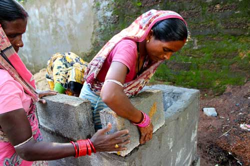 A woman carefully lays a block on top of wet cememnt, creating a wall