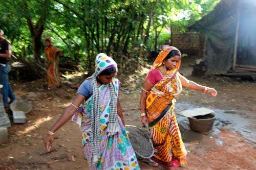 Two women, wearing colorful saris, carry a vessel filled with construction materials