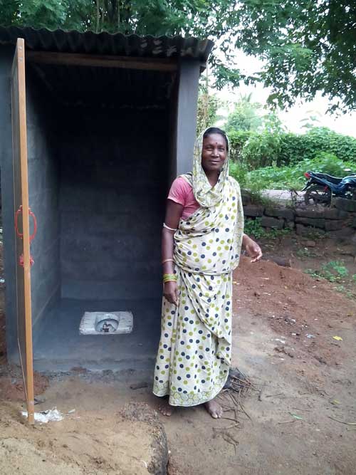 An Indian woman stands proudly in front of a newly constructed toilet