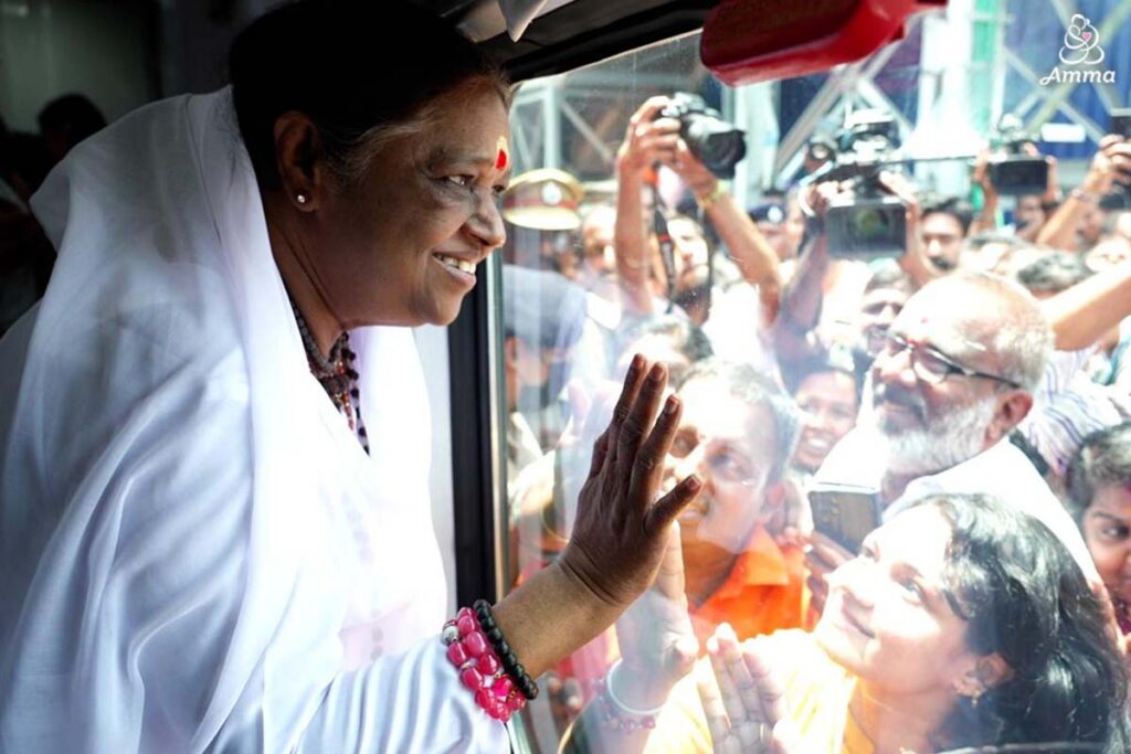 Amma looks out of a train window at a crowd with smiles