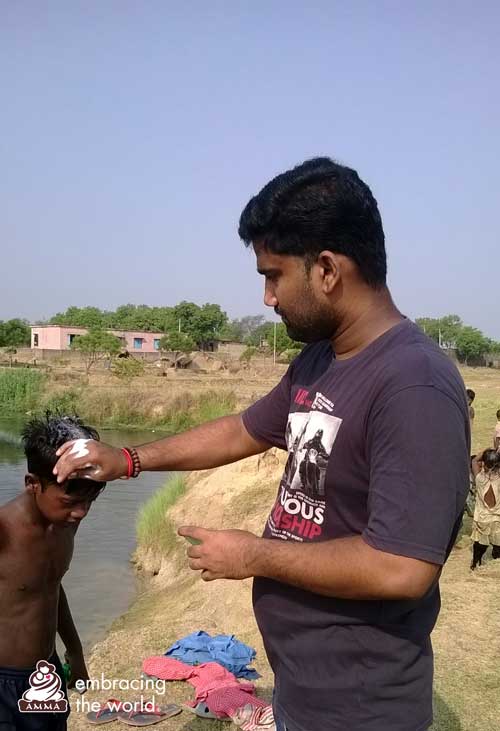 A child bathes in a river while volunteer puts shampoo in his hair