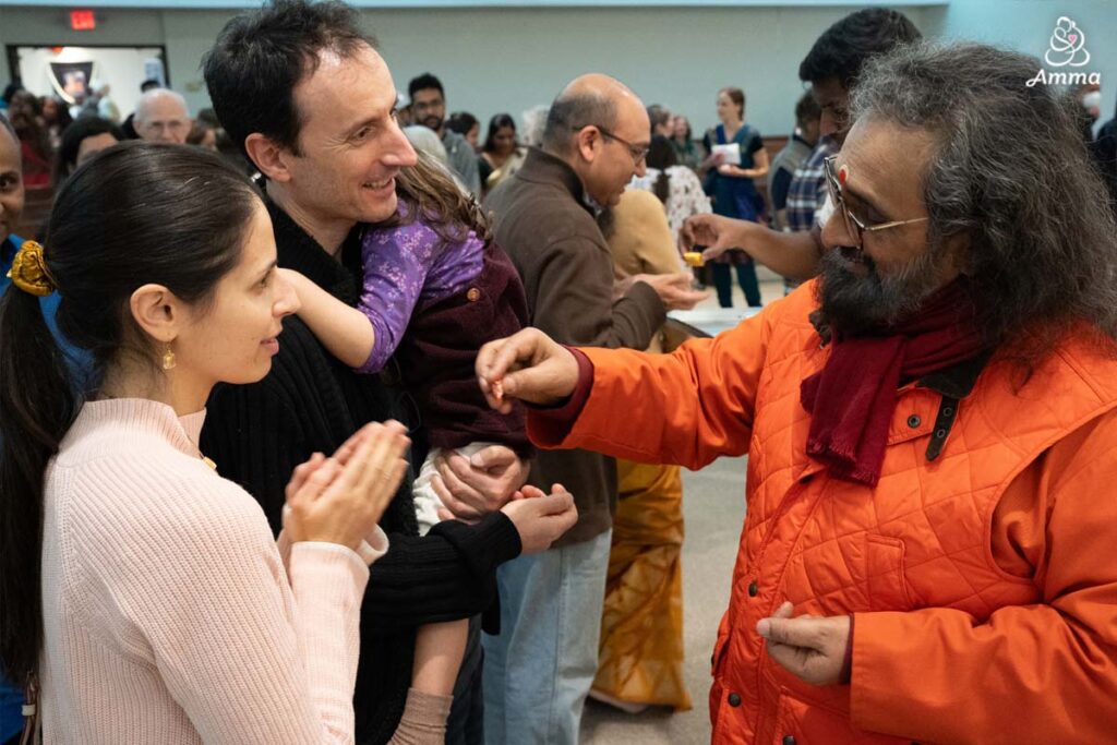 a Swami gives prasad to a mother, father, and child