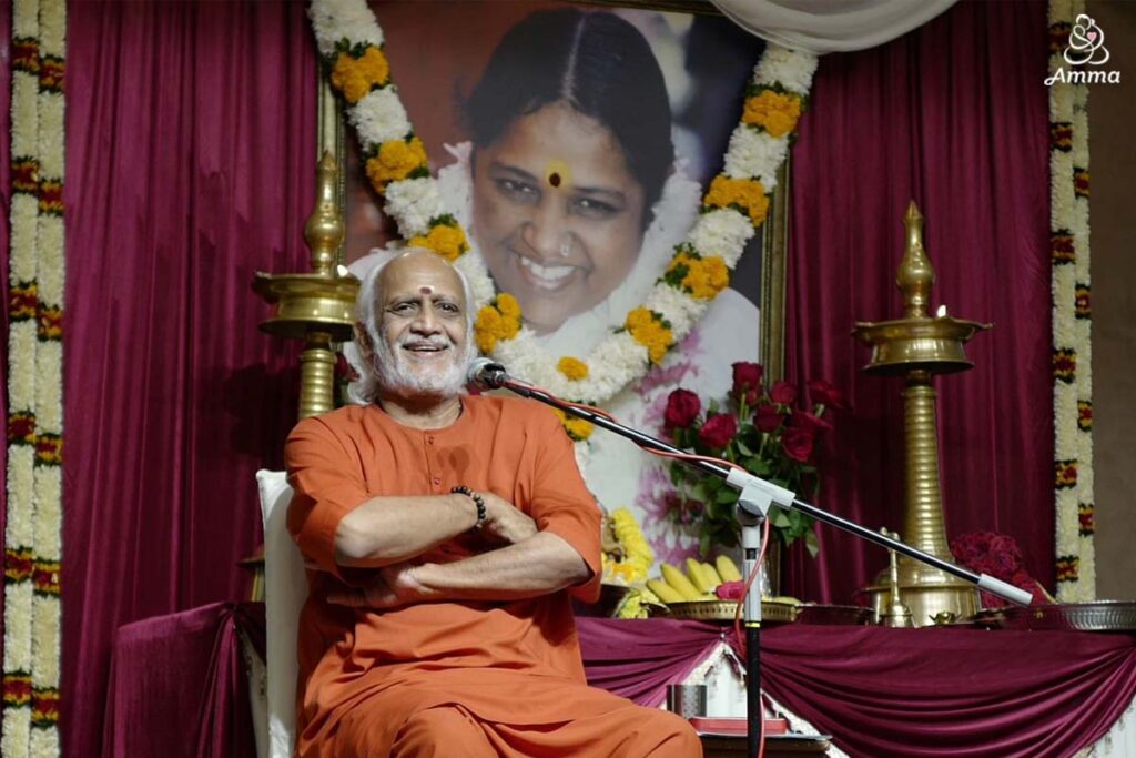 a Swami smiles in front of a photo of Amma