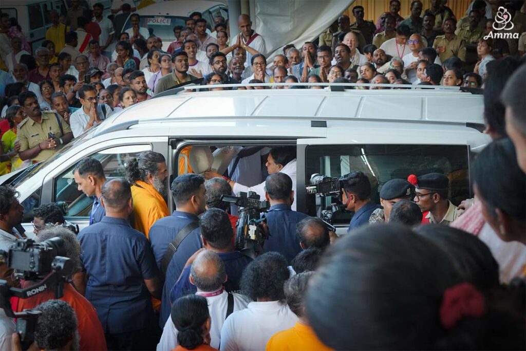Amma amidst a crowd of people around a car