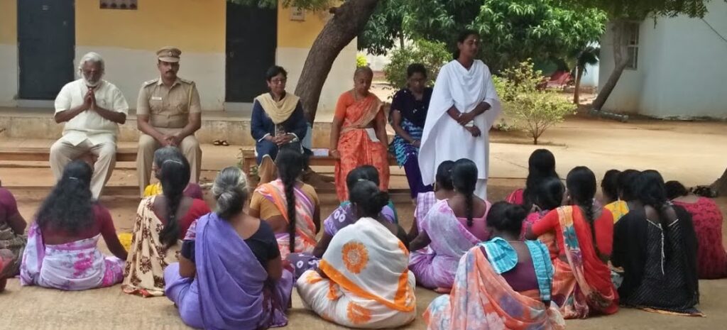 female prisoners sit outdoors and listen to ashram volunteers