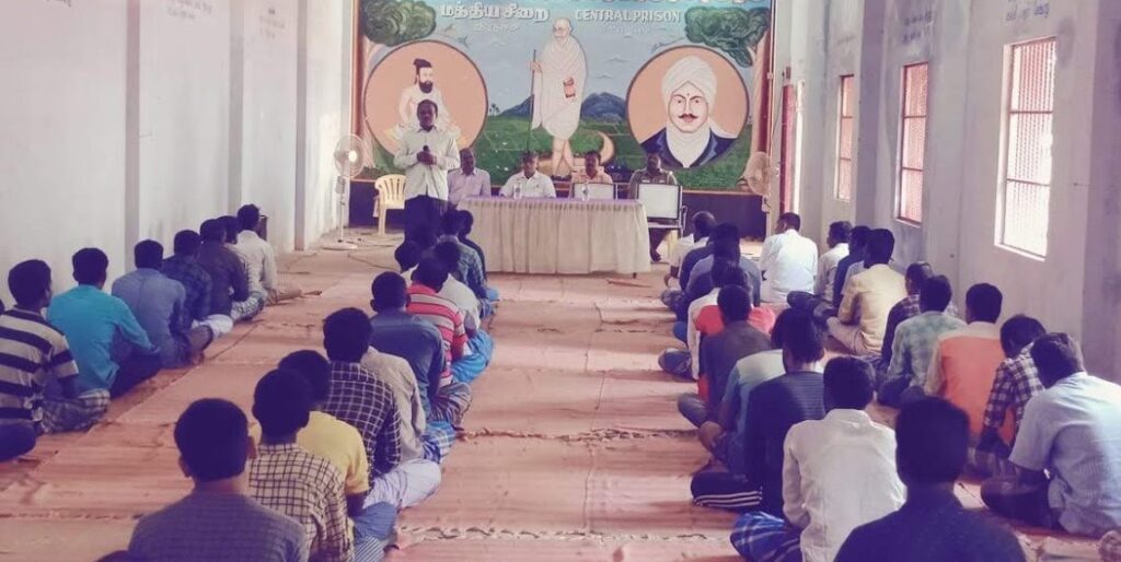 prisoners sit in a large hall and listen to ashram volunteers