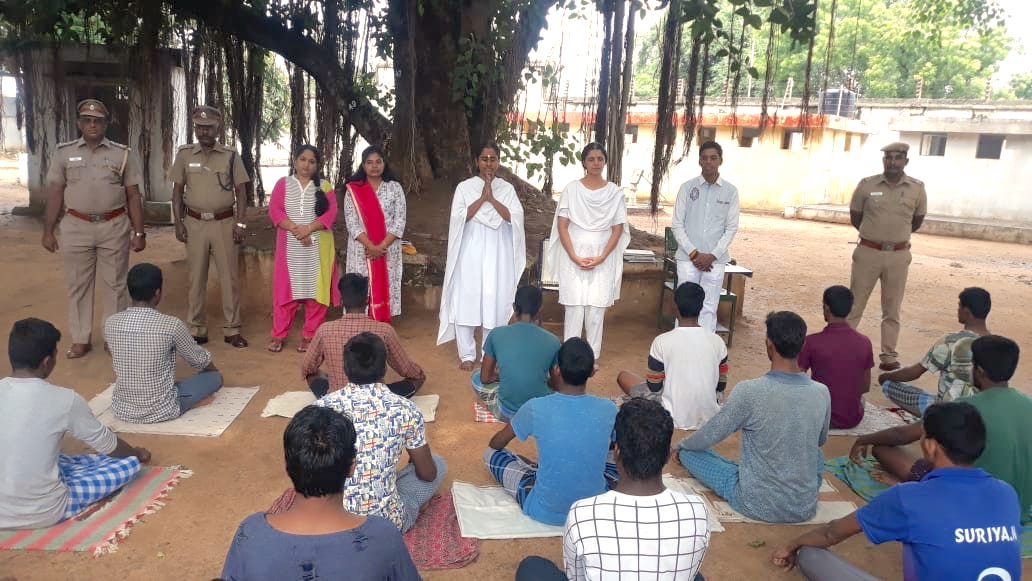 Prisoners sit outdoors and listen to ashram volunteers teach